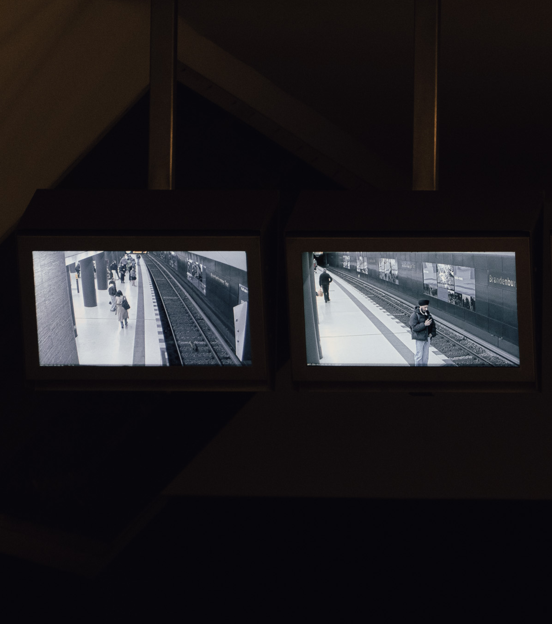 Two monitors displaying black-and-white footage of BVG U-Bahn platforms with commuters waiting